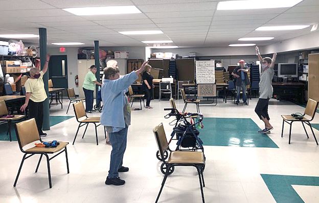 Several senior citizens mimic the instructor during Chair Exercise Class in the basement of the Earl